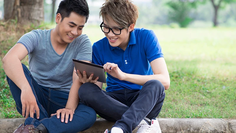 Two teens sitting on a curb reading a tablet