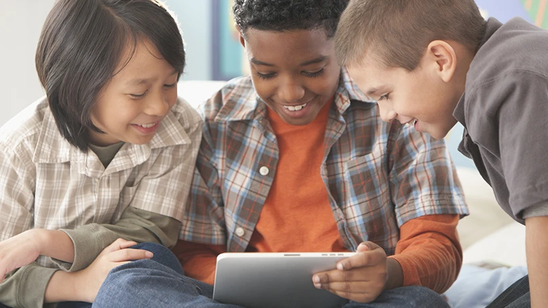 Three children reading computer tablet